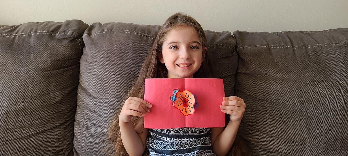A young smiling girl holding her handmade popup card.
