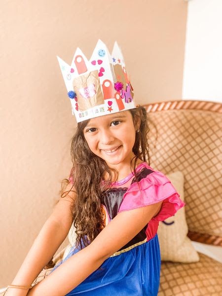 A smiling girl wearing an orange and white crown, and in a "Frozen" costume.