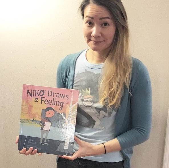 A photo of Simone Shin holding her picture book, Niko Draws a Feeling.