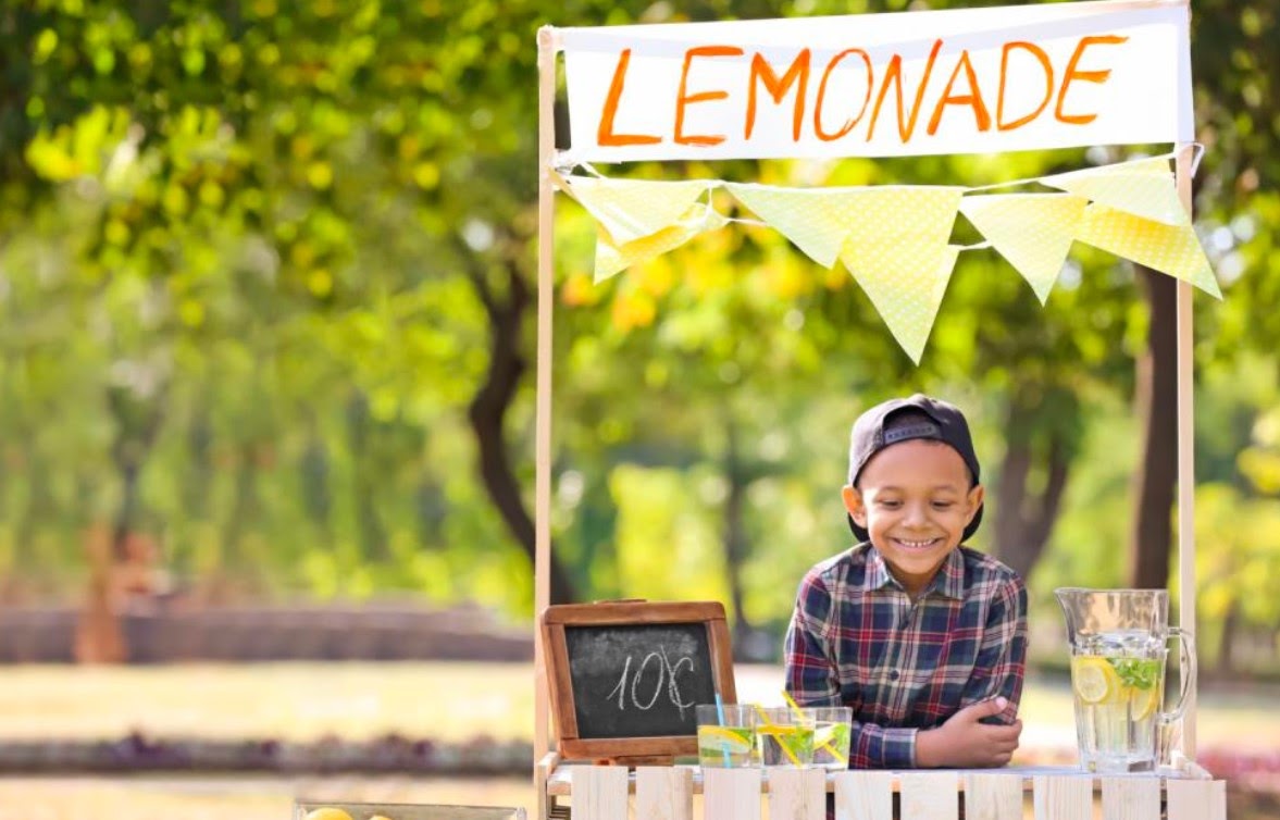 Young boy smiling while selling lemonade in a stand